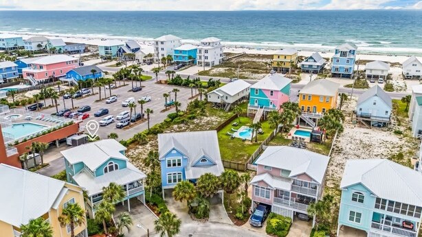 Zona residencial costera con casas coloridas, una piscina y una playa al fondo.