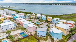 Zona residencial costera con casas coloridas, una piscina y un muelle al fondo.