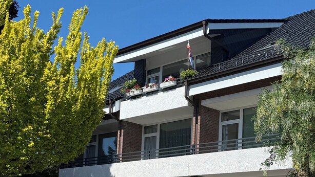 A multi-story building with balconies, windows, and a flag.