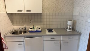 A compact kitchen with white cabinets, a stainless steel sink, a coffee maker, and a dish drying rack.