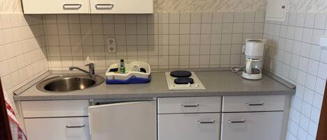 Una cocina compacta con armarios blancos, un lavamanos de acero inoxidable, una cafetera y un escurreplatos.