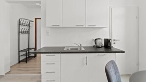A modern kitchen with white cabinets, a black countertop, a sink, a kettle, and a chair. - Faraway Homes Studios St.Michael (Liesingtal)