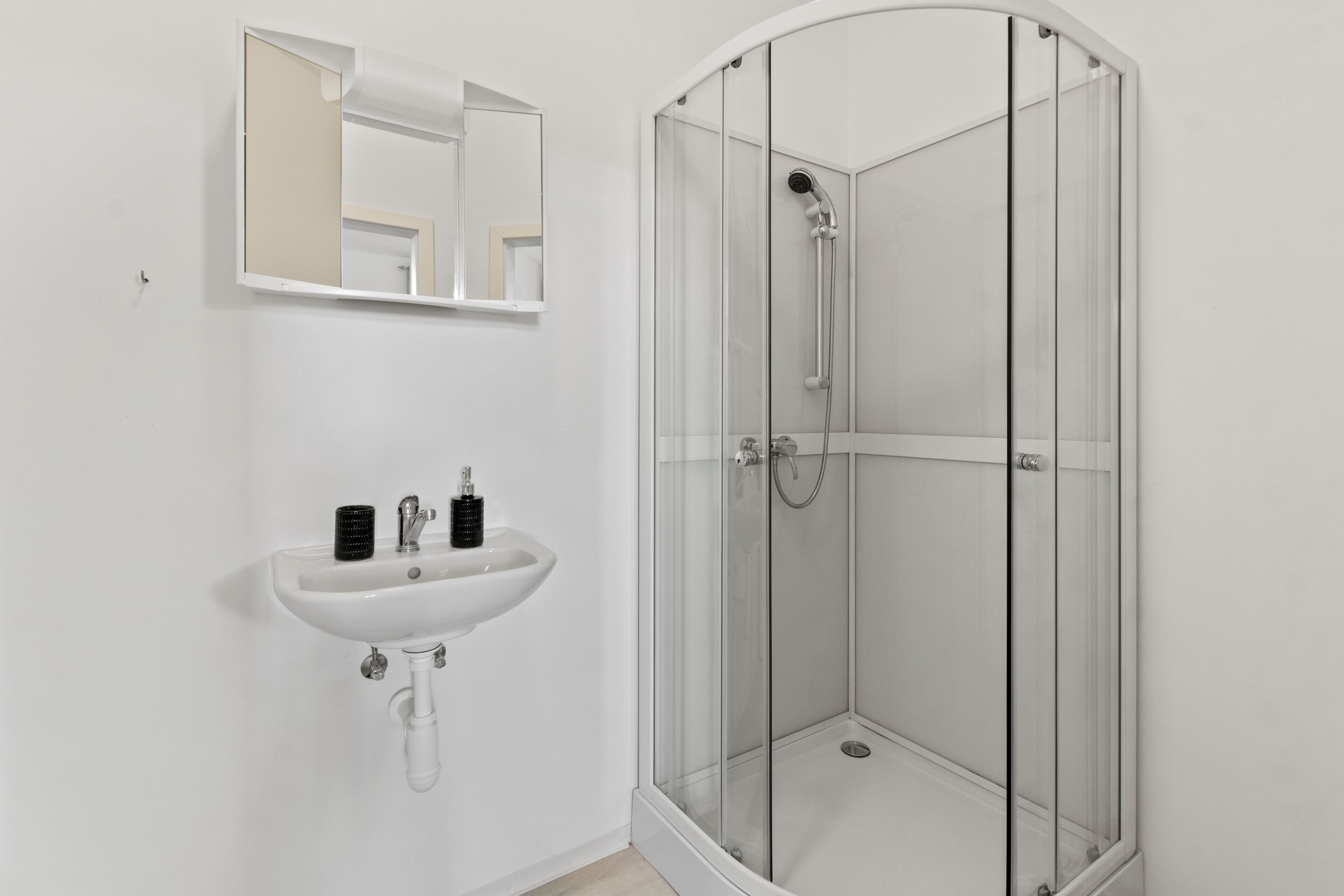 A bathroom with a white sink, a mirror, and a glass-enclosed shower.