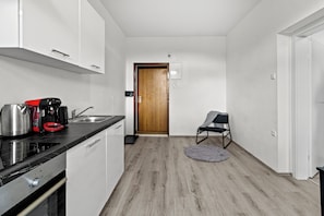 Une cuisine moderne avec un plan de travail noir, une machine à café et une bouilloire. Une porte en bois donne accès à une autre pièce.