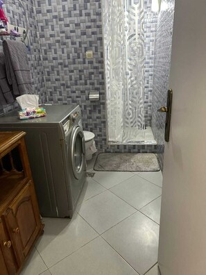 A compact bathroom with a washing machine, toilet, and shower area. - Agadir city center apartment (Agadir)