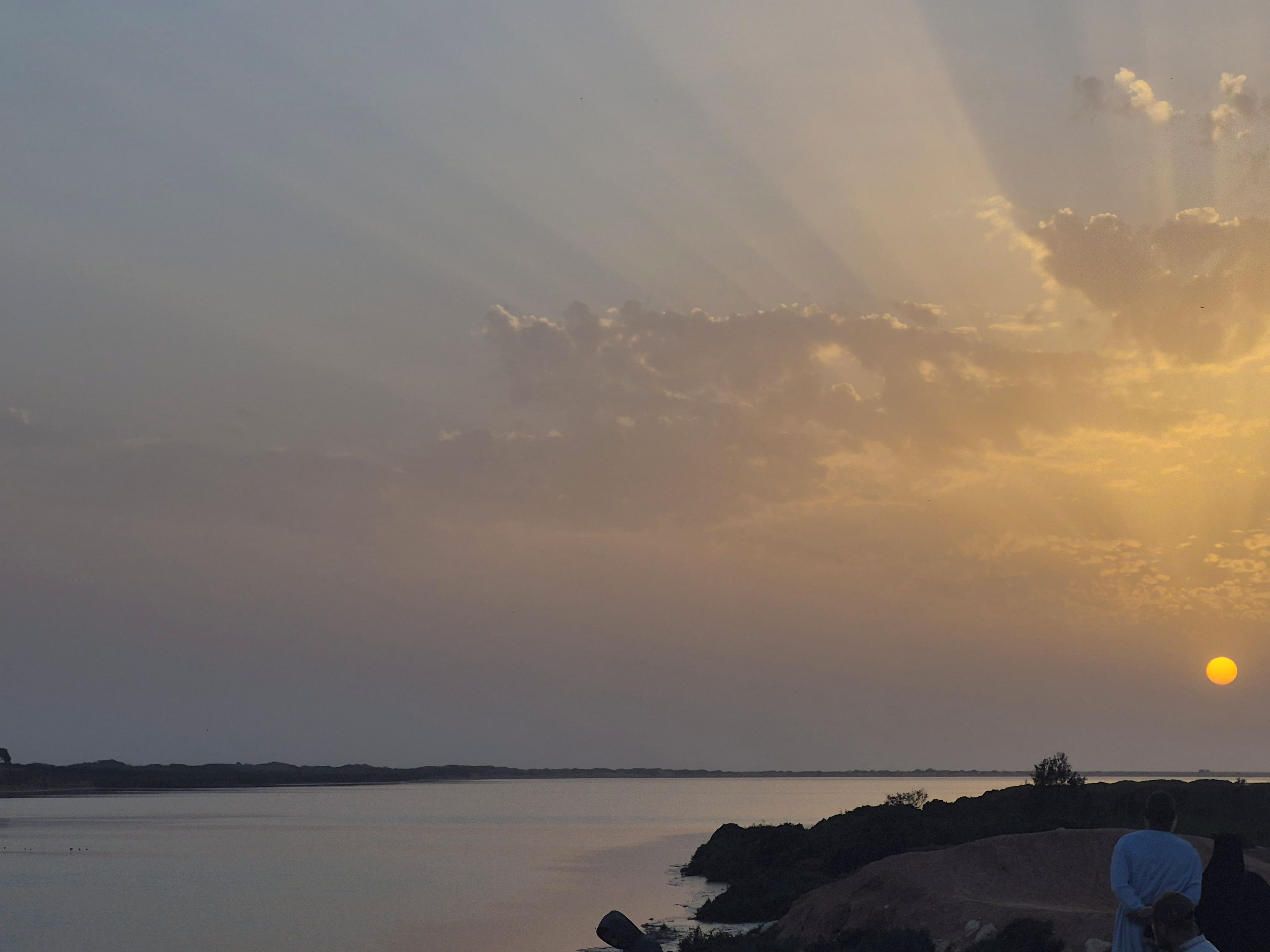 A sunset over a body of water with a rocky shoreline.