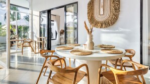 A dining area with round tables, wooden chairs, woven placemats, and a wall-mounted woven tapestry. - Villa AMARÉ New Stylish 3BR Canggu Large Pool,
Cinema & BBQ (Badung)
