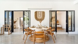 A dining area with a round table, wooden chairs, and a woven mat. - Villa AMARÉ New Stylish 3BR Canggu Large Pool,
Cinema & BBQ (Badung)