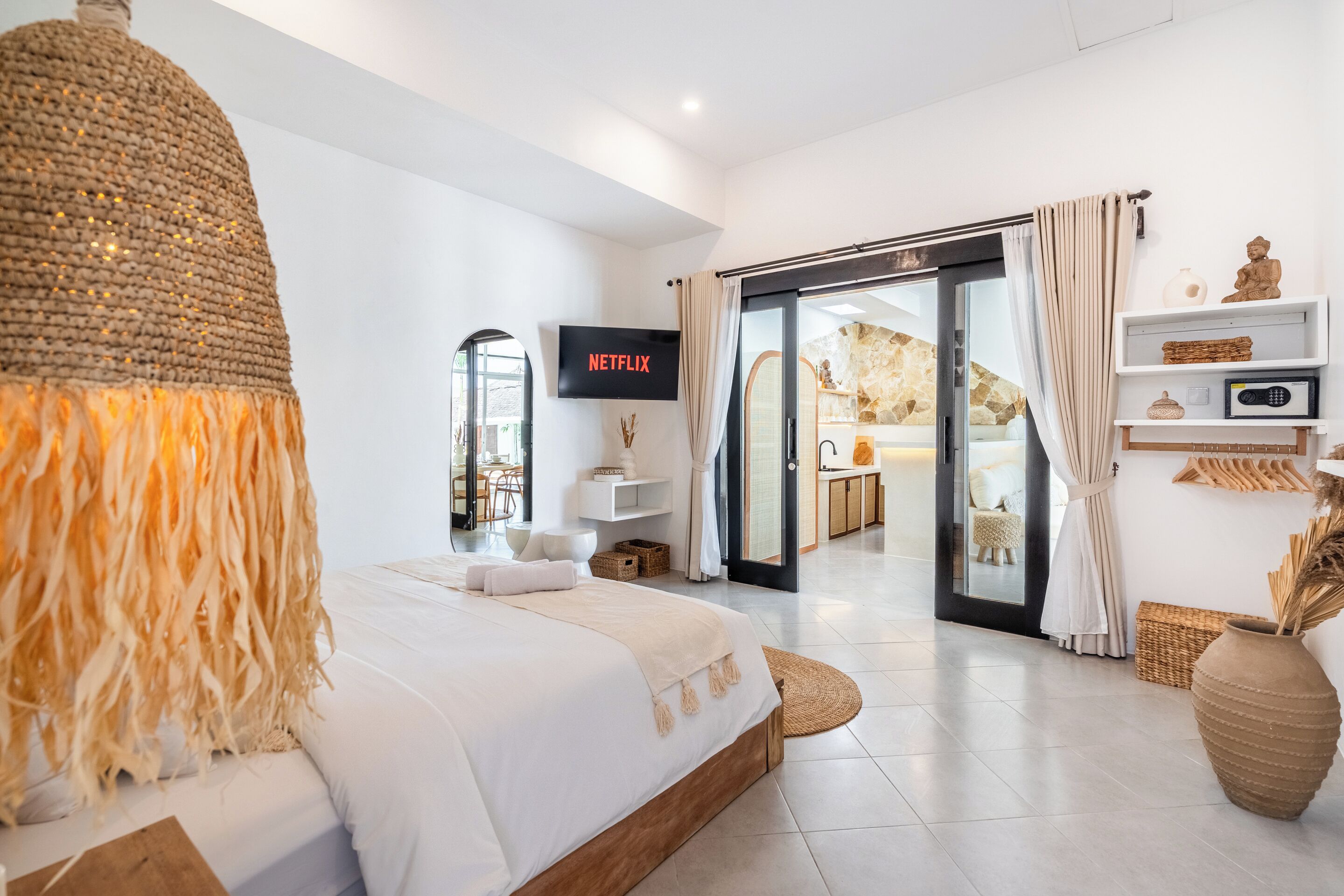 A modern hotel room with a large bed, a television, a sliding glass door to a balcony, and a minimalist decor.