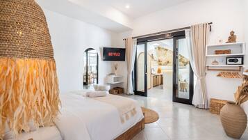 A modern hotel room with a large bed, a television, a sliding glass door to a balcony, and a minimalist decor.