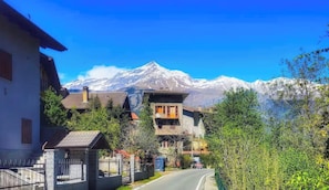 Une route de montagne, avec des maisons et un sommet enneigé en arrière-plan.