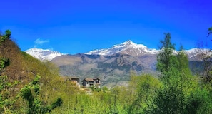 Un paysage de montagne avec des sommets enneigés, un ciel bleu dégagé et une maison nichée au milieu des arbres.