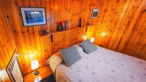 A wooden-paneled room with a bed, two bedside lamps, a shelf with books, and framed pictures on the wall. - Belvedere House at the foot of the mountains, welcome our 4-legged friends (Gravere)