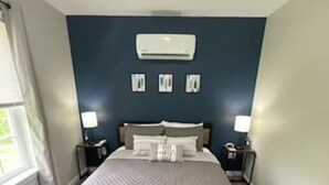 Ein Schlafzimmer mit einem Bett, Nachttischen, einer Klimaanlage und gerahmten Bildern an der Wand.