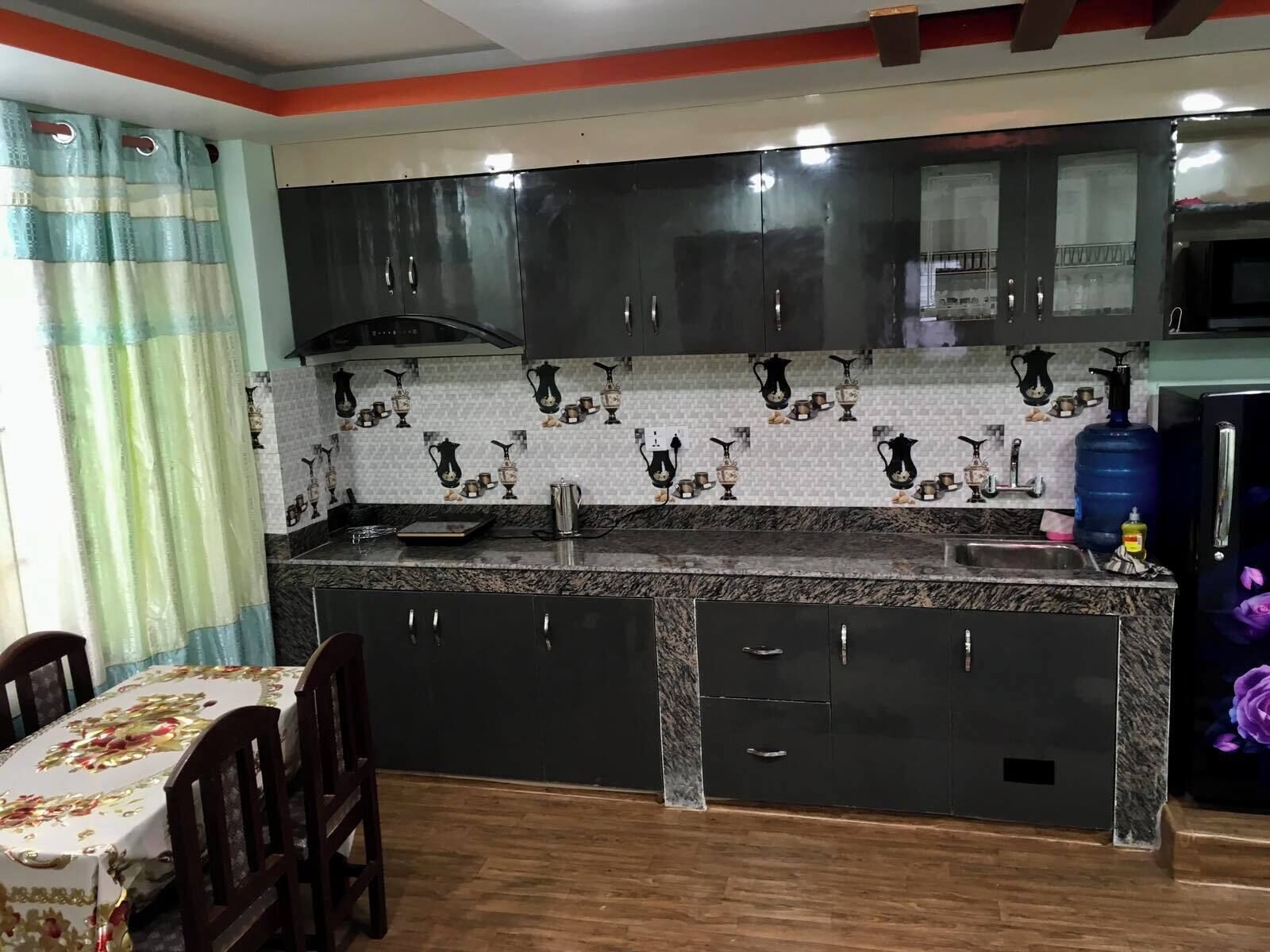 A kitchen with dark cabinets, a marble countertop, and a backsplash with kitchenware designs.