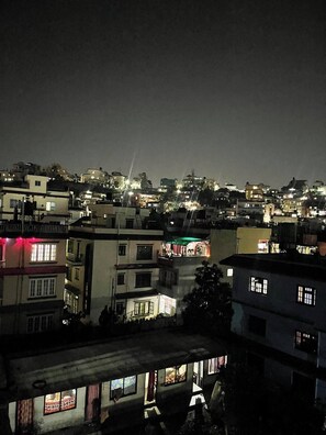 Vista nocturna de una zona urbana densamente poblada con edificios iluminados y una estructura verde destacada en el centro.