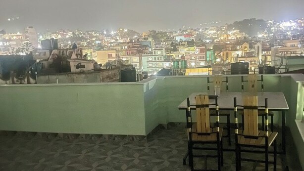 A rooftop terrace with a table and chairs, overlooking a cityscape at night. - Full Furnished 2BHK (Kathmandu)