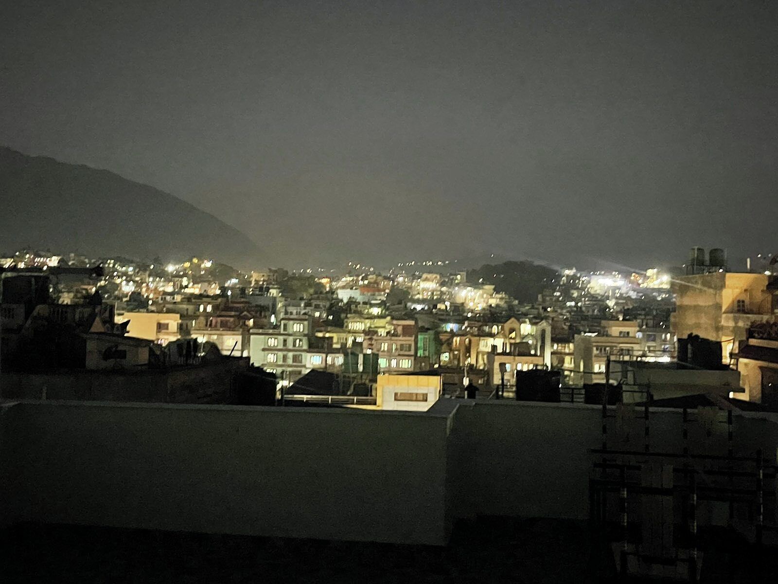 A nighttime cityscape with illuminated buildings and a mountain in the background.