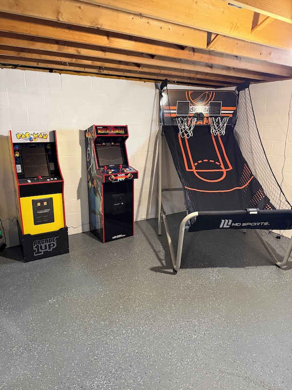 Spielautomaten, ein Basketballkorb und eine Holzbalkendecke in einem Raum.