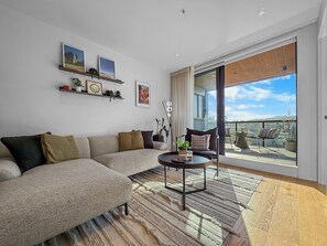 Un salon moderne avec un canapé, une table basse et une vue sur la ville grâce à de grandes fenêtres.