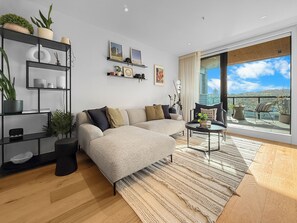 A modern living room with a sofa, coffee table, and a view of a cityscape through large windows. - Onehunga Sanctuary I 2-Bed Apt. I Amazing Views (Grey Lynn)