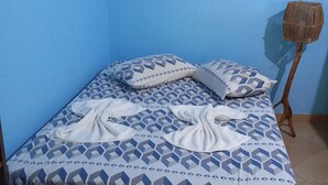 Een enkel bed met een gebedrukte spreidek, een wanddecoratie en een klein houten krukje.