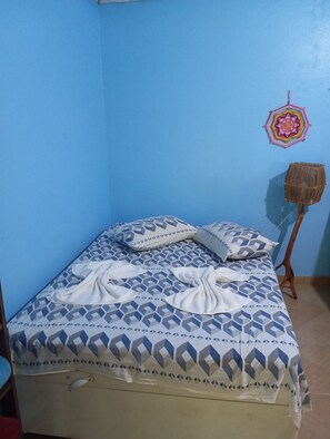 A single bed with a patterned bedspread, a wall hanging, and a small wooden stool.