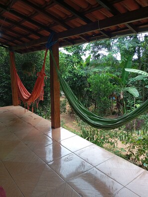 A covered patio area with a hammock, tiled flooring, and a view of a lush garden.