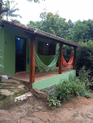 A green house with a porch, a hammock, and a cat.