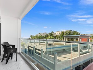 Ein Balkon mit Glasgeländer, einem Stuhl und Blick auf Gebäude und Palmen.