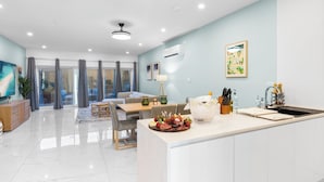 A modern kitchen with a central island, a dining area with a table and chairs, and a living space with a sofa and a TV. - Nirvana - Stay Steps from the Sand in Simpson Bay (Simpson Bay)