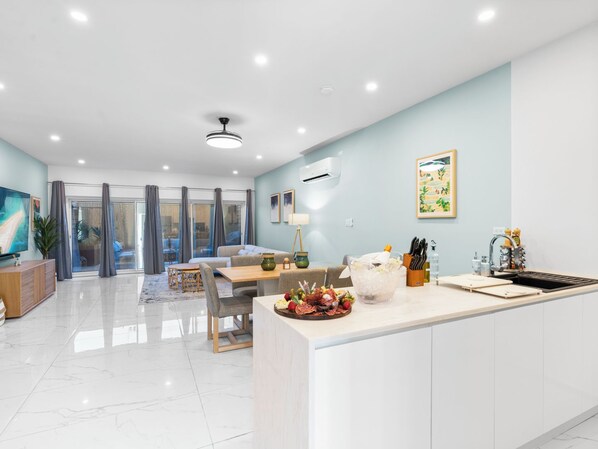 A modern kitchen with a central island, a dining area with a table and chairs, and a living space with a sofa and a TV. - Nirvana - Stay Steps from the Sand in Simpson Bay (Simpson Bay)