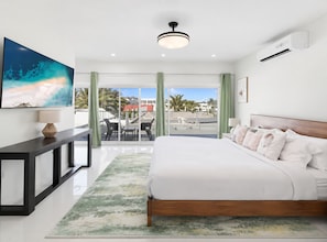 Habitación de hotel moderna con una cama grande, un escritorio, un televisor y un balcón con vista a palmeras y edificios.