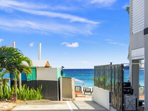 Ein Küstenanwesen mit Blick auf den Strand, einer umzäunten Terrasse und einem kleinen Gebäude mit einer Tür.