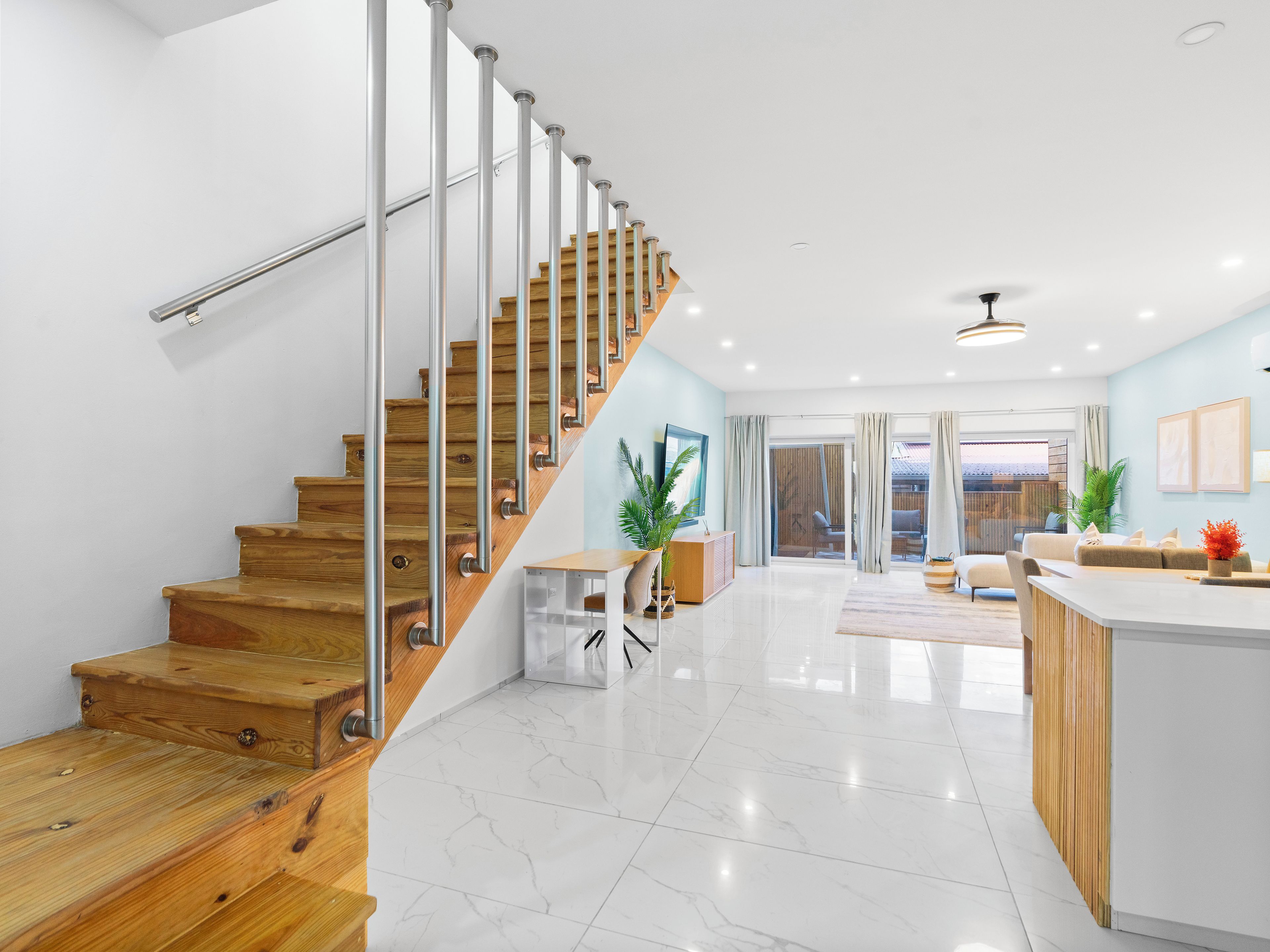 A modern interior with a wooden staircase, a kitchen area, and a living space with a view.