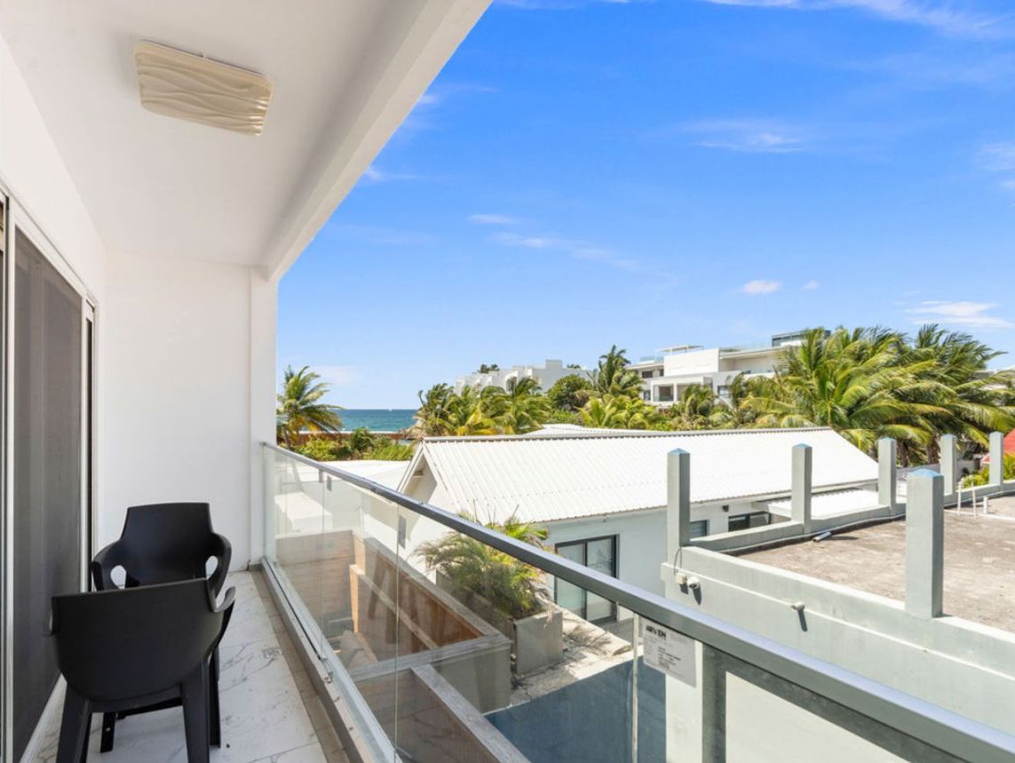 A balcony with a clear view of the ocean and palm trees.