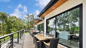 Eine Terrasse mit Gartenmöbeln, großen Fenstern und Blick auf Bäume.