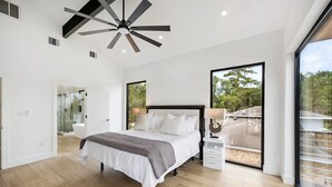 Ein modernes Schlafzimmer mit einem großen Bett, einem Deckenventilator, einer Glasdusche und einem Balkon mit Aussicht.