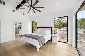 Ein modernes Schlafzimmer mit einem großen Bett, einem Deckenventilator, einer Glasdusche und einem Balkon mit Aussicht.