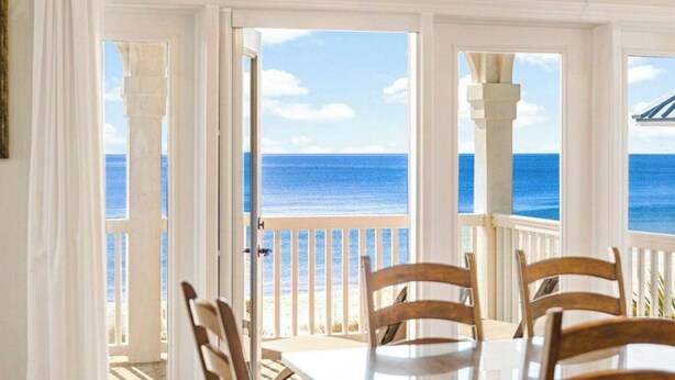 A dining area with a view of the ocean, white walls, and wooden chairs. - Beach Front- St George Island -Pool -Game Room (Saint George Island)