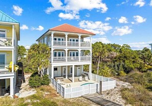 Ein zweistöckiges Strandhaus mit Balkon, Pool und Holzterrasse.