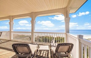 Eine überdachte Terrasse mit weißen Geländern und Blick auf den Strand, ergänzt durch Liegestühle.