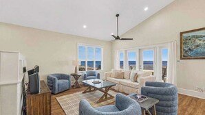A spacious living room with a sofa, armchairs, a coffee table, and a TV. There are large windows offering a view of the sea. - Beach Front- St George Island -Pool -Game Room (Saint George Island)