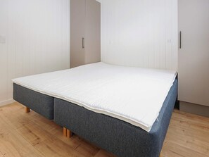 A minimalist bedroom with a single bed, wooden flooring, and white walls. - 5 Star Holiday Home in Hals (Hals)