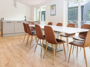 Eine moderne Küche mit weißen Schränken, einer großen Kochinsel und einem Essbereich mit weißem Tisch und braunen Stühlen.
