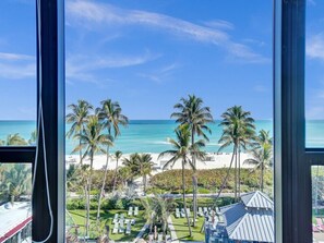 Blick aus einem Fenster auf einen Strand mit Palmen und einem strahlend blauen Himmel.