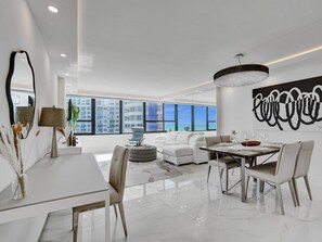 Una sala de estar moderna con comedor, ventanas amplias, una araña y vista a la ciudad.