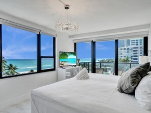 Ein Schlafzimmer mit einem großen Bett, einer Kristallleuchter, einem Fernseher und Blick aufs Meer.