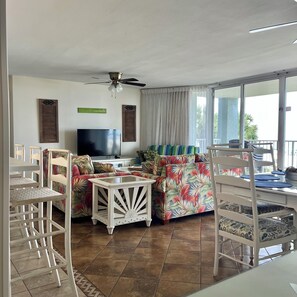 A living room with a TV, a ceiling fan, a sofa, and a dining area with chairs and a table. - Amazing view @ Long Beach Resort Tower-1 (Panama City Beach)