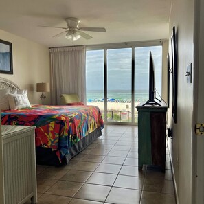 Une chambre d’hôtel avec un lit, un ventilateur de plafond, une télévision, un bureau et une vue sur la plage.